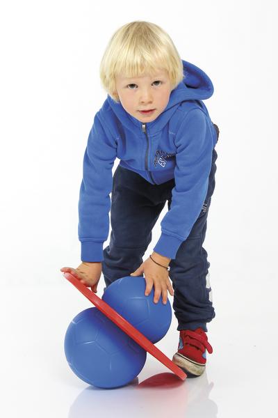Kleiner Junge in blauer Jacke spielt mit blauem Balance-Board und Ball auf weißem Hintergrund.
