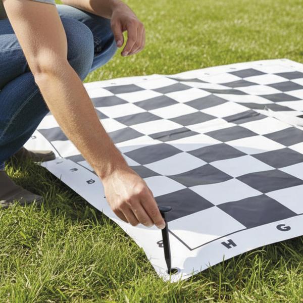 Person befestigt ein großes Schachspielfeld im Gras mit einem Erdanker.