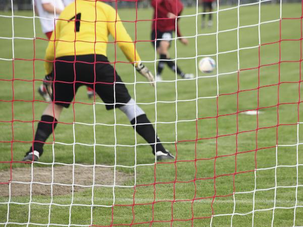 Torwart in gelbem Trikot bereitet sich auf Schuss im Fußballspiel vor, Ball im Anflug.