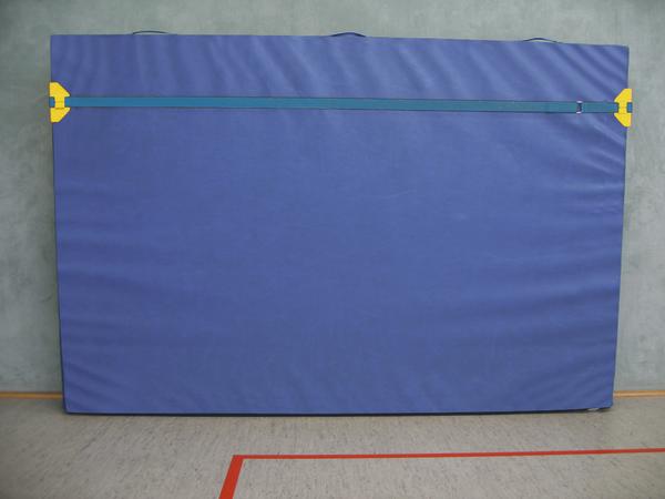 Blauer Turnmattenbezug mit Reißverschluss, an Wand in Sporthalle befestigt.