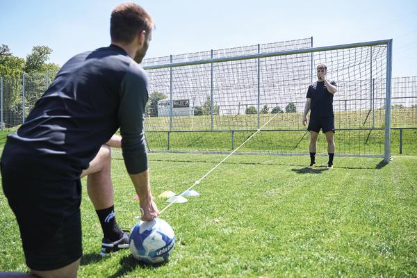 Fußballtraining mit Widerstandsband auf dem Sportplatz vor einem Fußballtor.
