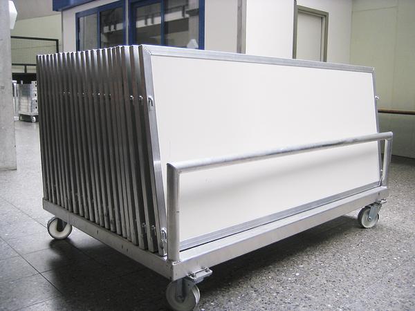 Transportwagen mit mehreren weißen, rechteckigen Tafeln auf Rollen in Innenraum.