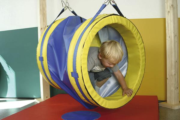 Kind spielt in hängendem, buntem Tunnel im Indoor-Spielbereich auf roter Matte.