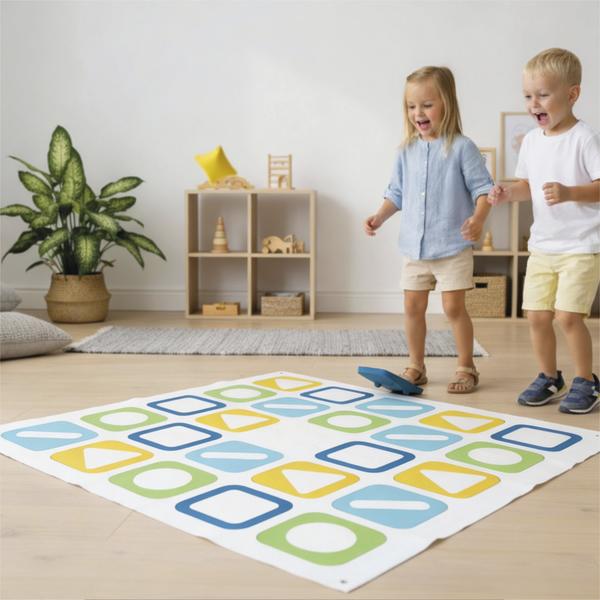 Zwei Kinder spielen auf einer großen Spielmatte mit farbigen Formen in einem Raum.