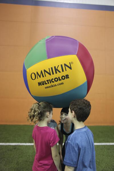 Kinder spielen mit einem bunten Omnikin-Multicolor-Ball in einer Sporthalle.
