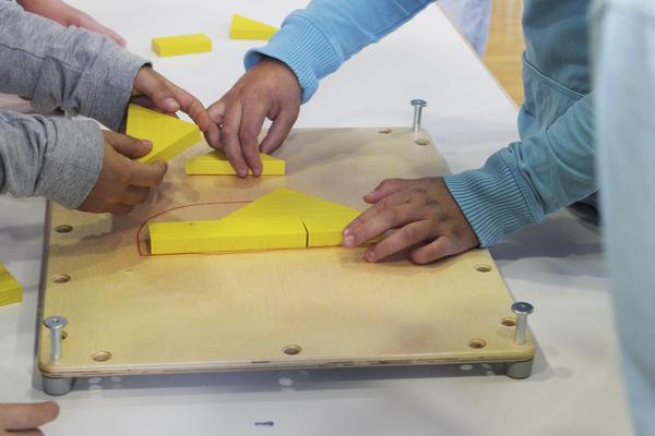 Kinderhände legen gelbe Holzpuzzleteile auf ein Holzbrett mit Aussparungen.