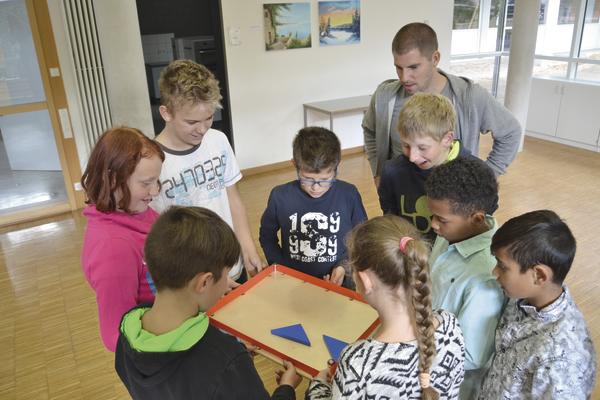 Kinder und Lehrer spielen gemeinsam ein Lernspiel mit geometrischen Formen in der Schule.