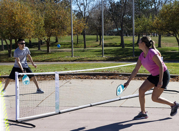 Frau und Mann spielen Pickleball im Park an sonnigem Herbsttag.