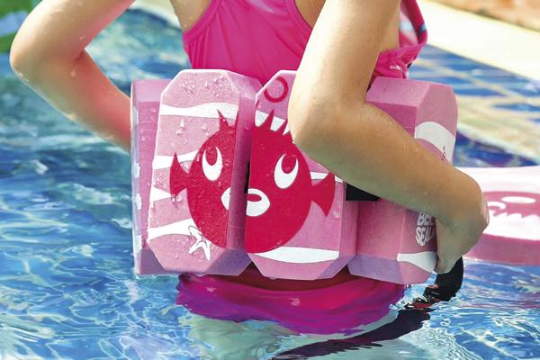 Kind mit pinkem Schwimmgürtel mit Fischmotiv im Schwimmbecken, Nahaufnahme.