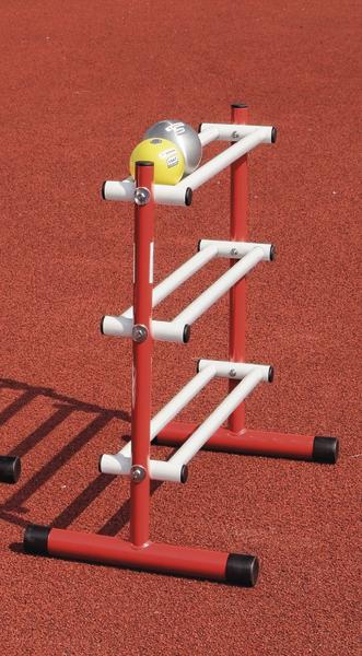 Rotes und weißes Sportgerät mit Medizinbällen auf rotem Laufbahnbelag.