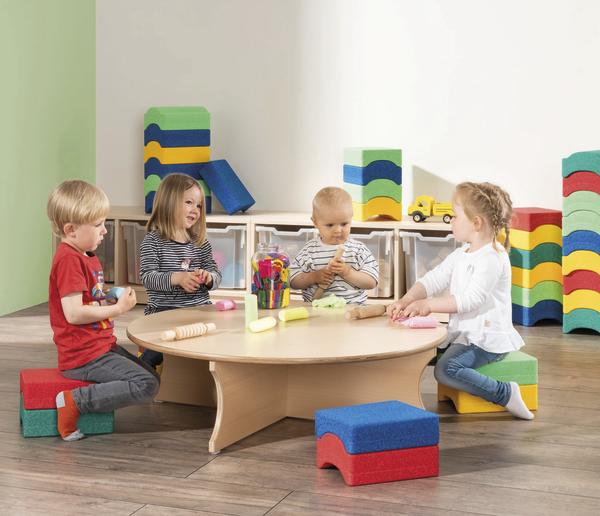 Vier Kinder sitzen an einem runden Tisch und spielen mit Knete; sie sitzen auf bunten Schaumstoffhockern.
