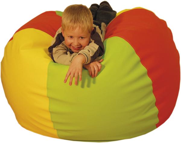 Kind liegt lachend auf buntem Sitzsack in Rot, Gelb und Grün, spielerisch und entspannt.