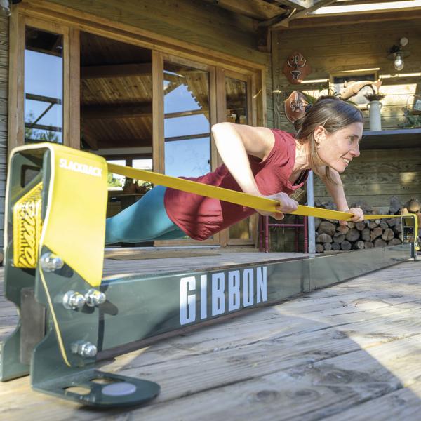 Frau trainiert mit Gibbon Slackrack Slackline-Trainingsgerät auf Holzterrasse vor Haus.