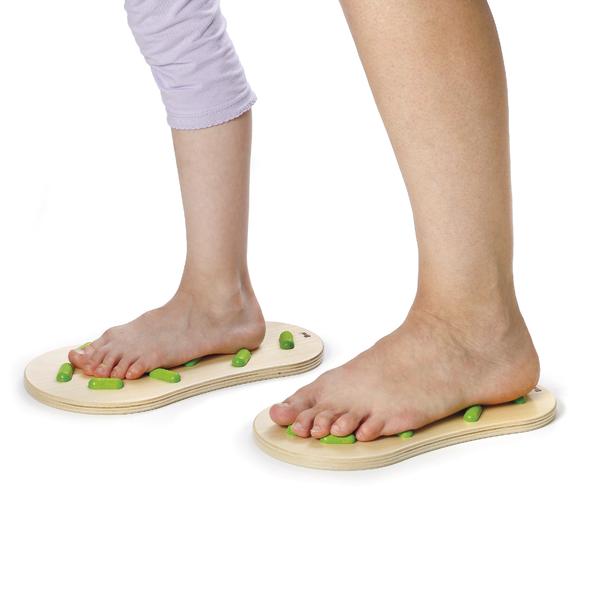 Barfuß auf Holz-Fußmassageplatten mit grünen Noppen zur Fußreflexzonenmassage stehend.