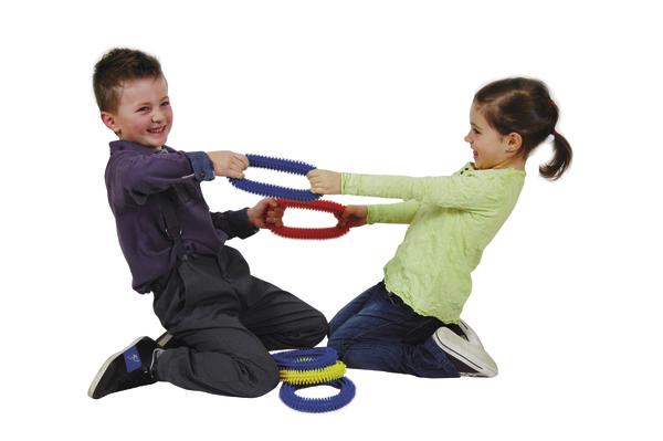 Junge und Mädchen spielen lachend mit bunten Greifringen auf weißem Hintergrund.
