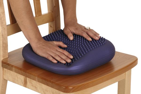 Ergonomisches Sitzkissen mit Noppen zur Druckentlastung auf Holzstuhl, Hände drücken es.