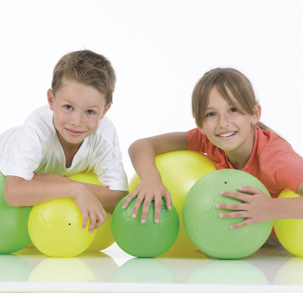 Junge und Mädchen liegen lächelnd mit bunten Gymnastikbällen auf weißem Hintergrund.