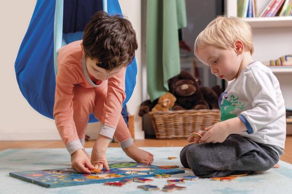 Zwei Kinder spielen gemeinsam mit einem Puzzle auf dem Boden in einem Kinderzimmer.