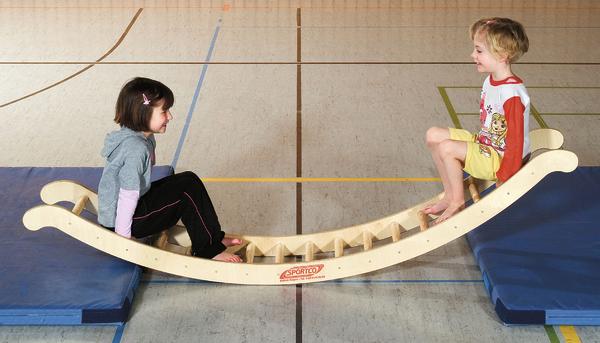 Kinder spielen auf einer Wippe aus Holz in einer Turnhalle mit blauen Matten.