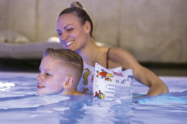 Frau unterstützt lächelnden Jungen mit Schwimmflügeln beim Schwimmen im Pool.