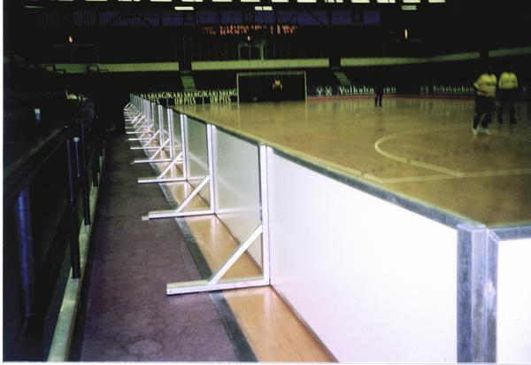 Innenaufnahme einer leeren Sporthalle mit Spielfeld und weißen Absperrungen am Spielfeldrand.
