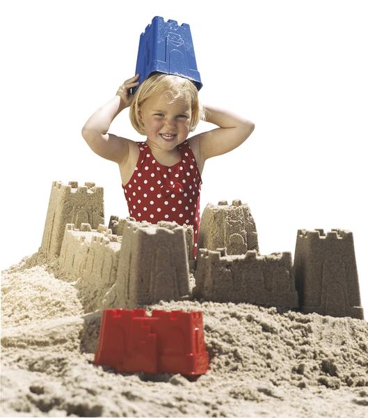 Kind spielt am Strand mit Sandburgen und trägt blauen Eimer als Hut, rotes Kleid mit Punkten.