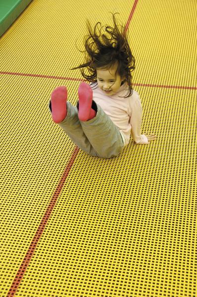 Kind spielt fröhlich auf einem großen gelben Trampolin mit roten Linien.