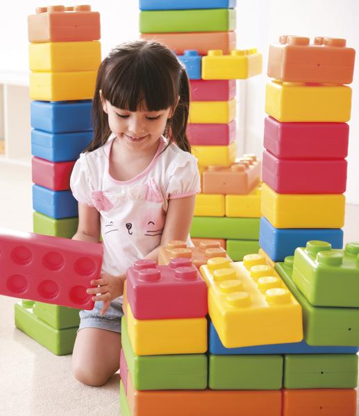 Mädchen spielt mit großen bunten Bausteinen und baut Türme im hellen Raum.