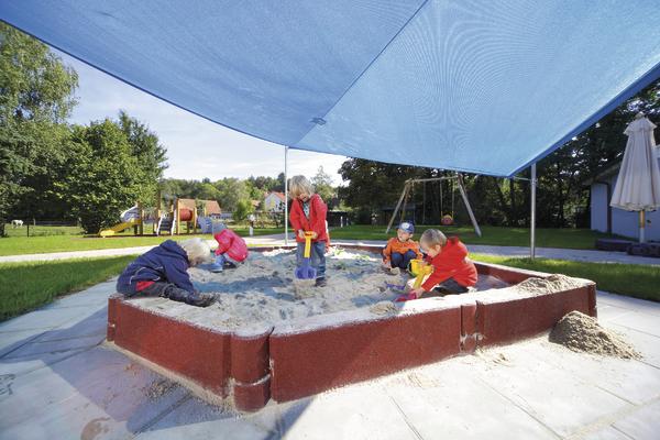 Kinder spielen im schattigen Sandkasten auf einem sonnigen Spielplatz im Freien.