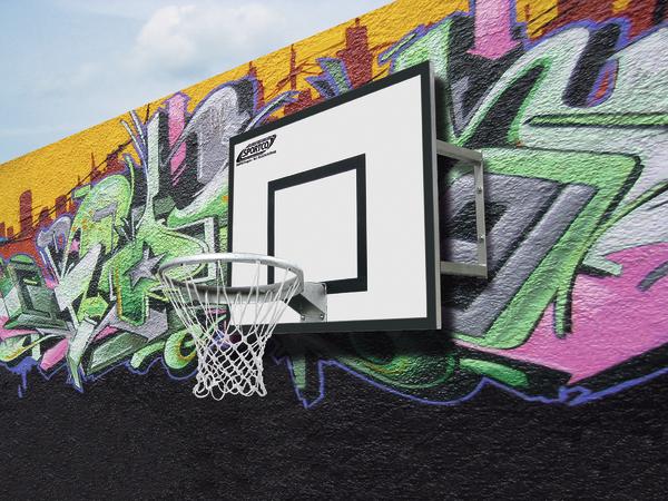 Basketballkorb an bunter Graffiti-Wand auf urbanem Outdoor-Spielfeld bei Tageslicht.
