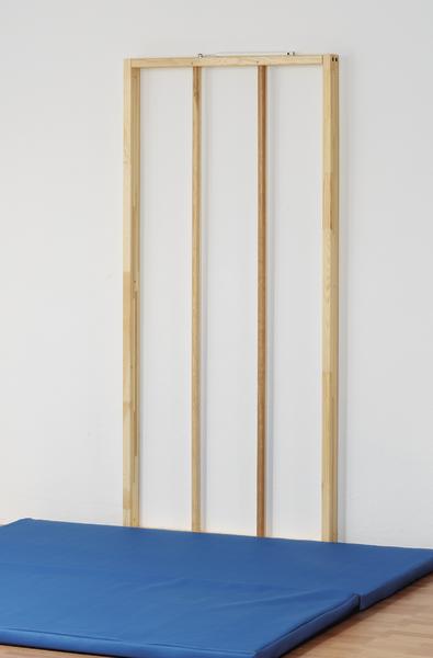 Holz-Kletterwand mit blauer Gymnastikmatte vor weißer Wand in Turnhalle.