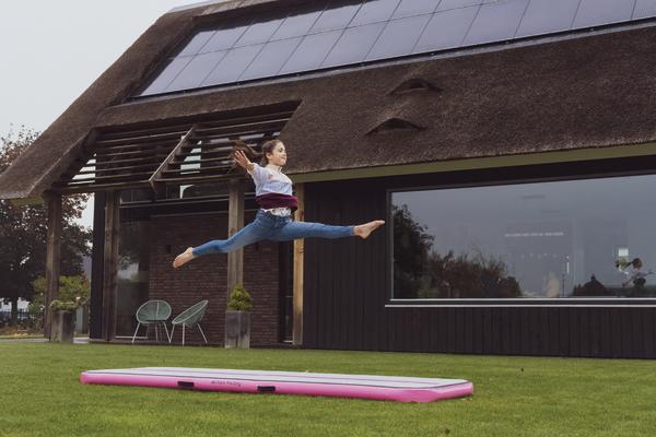 Mädchen springt auf aufblasbarer Airtrack-Matte vor modernem Haus mit Solarpanelen.
