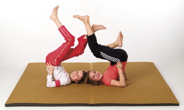 Kinder machen Gymnastik auf Matte, üben Schulterstand mit gestreckten Beinen.