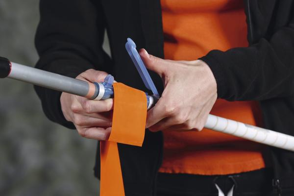 Person befestigt orangefarbenes Band an Nordic-Walking-Stab für Outdoor-Sport.