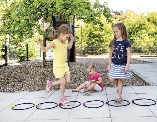 Kinder spielen draußen auf einem Spielplatz mit Reifen und springen fröhlich.
