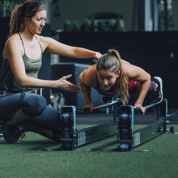 Frau macht Liegestütze mit Trainerin im Fitnessstudio für Krafttraining.