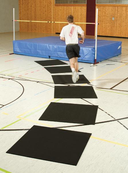 Junger Mann läuft in Halle auf Matten zu Hochsprungmatte für Training.