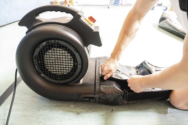 Person befestigt schwarzen Luftgebläse-Schlauch auf Werkstattboden.