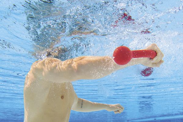 Unterwasseraufnahme eines Mannes, der mit roten Hanteln im Pool trainiert.