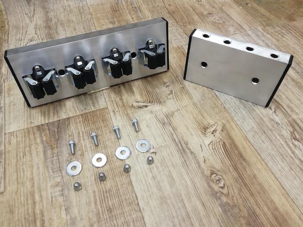 Metallhalterung mit vier schwarzen Klemmen und Montagematerial auf Holzboden.
