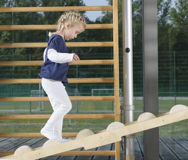 Kind balanciert auf Holzspielgerät im Freien, motorische Fähigkeiten trainierend.