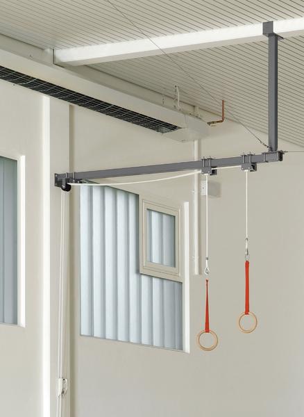 Turnringe mit roten Gurten hängen an einer Multifunktionsschaukel in einer hellen Sporthalle.