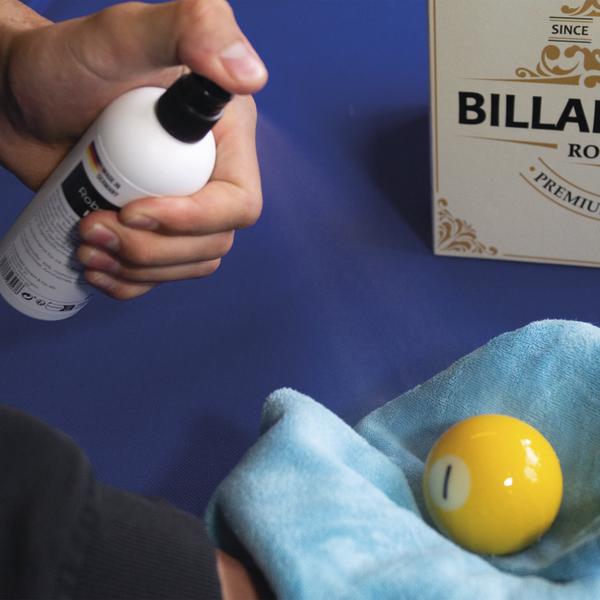 Hand sprüht Kugelreiniger auf Billardkugel im Tuch