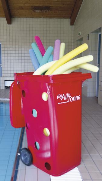 Roter Behälter mit bunten Schwimmnudeln am Schwimmbadrand in Hallenbad.