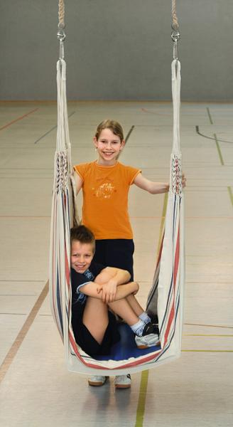 Zwei Kinder spielen gemeinsam in einer Hängematte in einer Sporthalle.