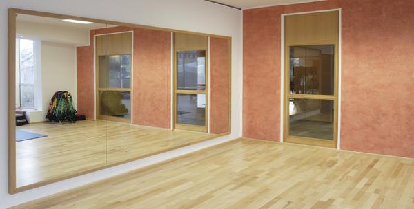 Moderner Tanzraum mit großem Wandspiegel und Holzboden, heller Trainingsbereich.
