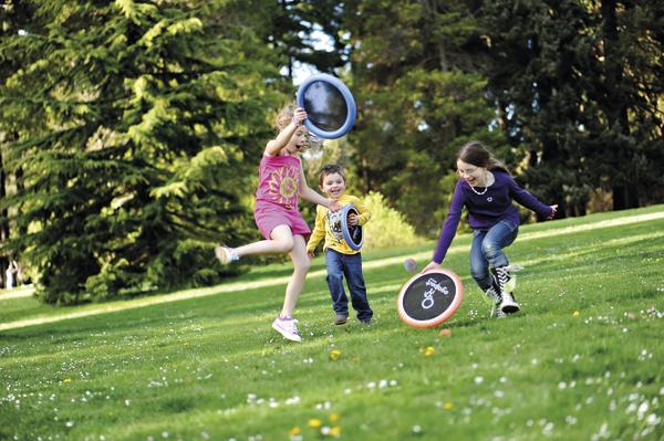 Drei Kinder spielen mit Wurfscheiben auf einer grünen Wiese im Park.