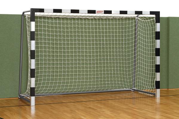 Handballtor mit Netz in Sporthalle auf Holzboden vor grüner Wand.