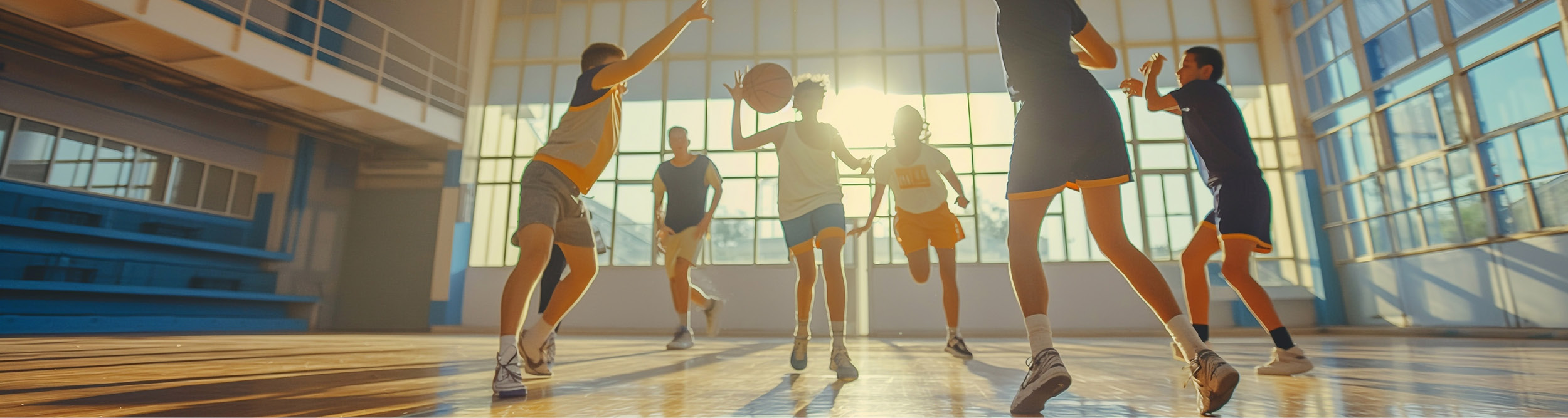 Jugendliche spielen Basketball in heller Sporthalle mit Sonnenlicht und Bewegung.