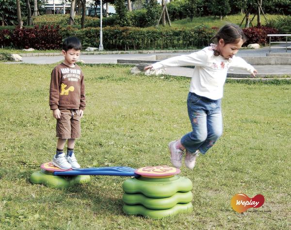 Kinder spielen draußen auf einem Balanciergerät im Park bei sonnigem Wetter.